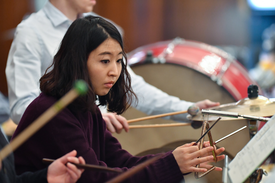 A student playing the triangle in the percussion section of the H漫画 Philharmonic.